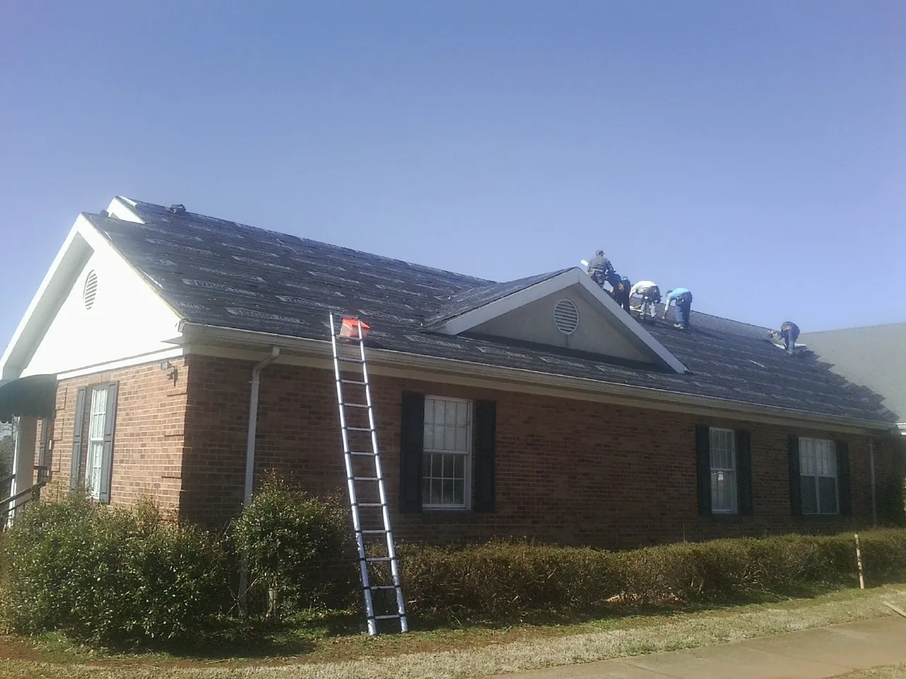 Crew tearing shingles off a brick ranch roof with a ladder set — Emergency Roof Repair work by our crew in Kimball