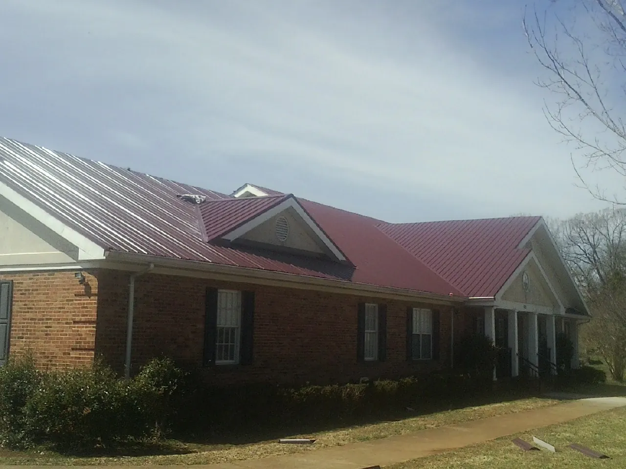 Red metal roof with gabled entries on a long brick building, from a Hail Damage Roof Repair job in Kimball