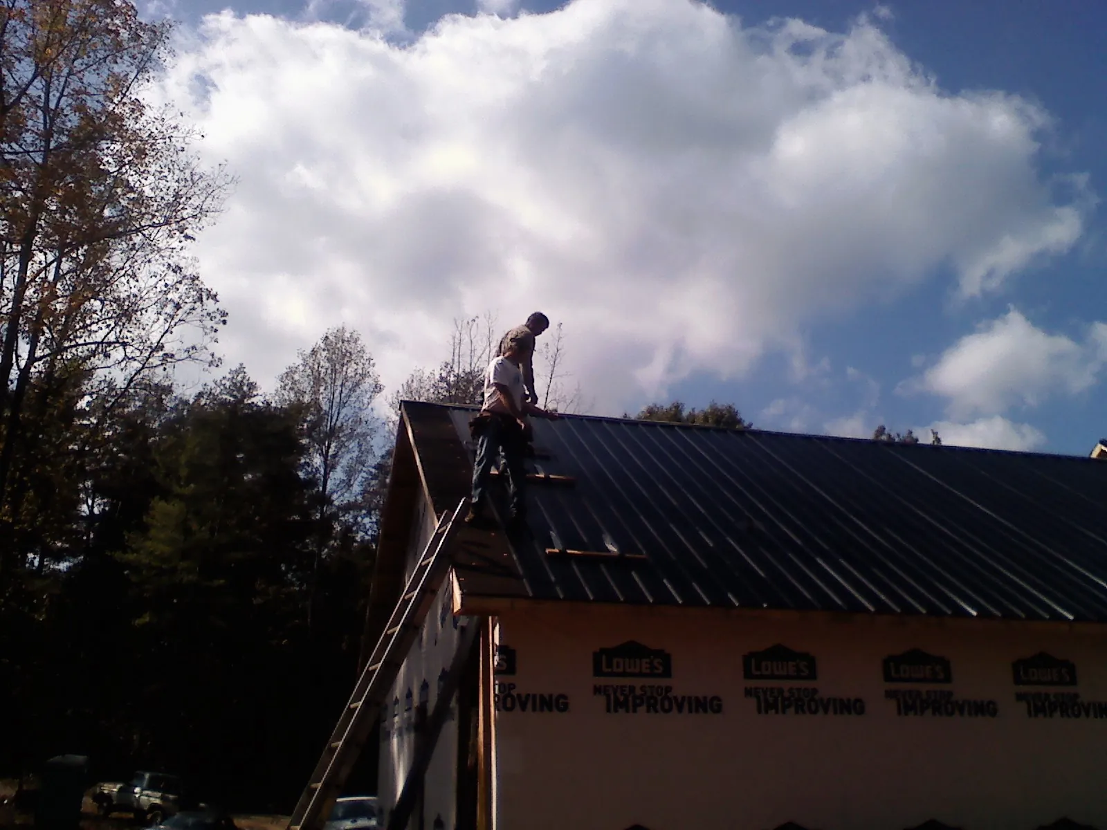 Roofer fastening dark metal panels high against a cloudy sky, from a Roof Inspection job in Kimball
