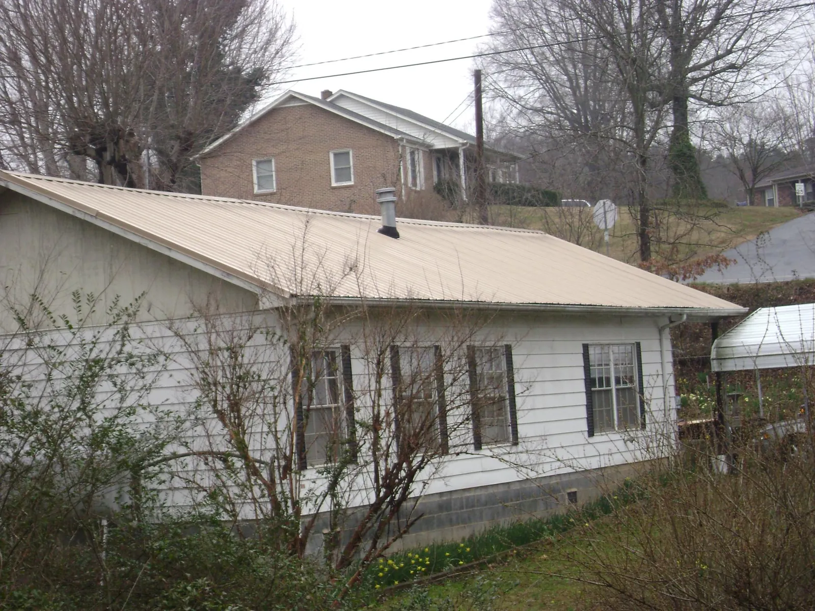 Tan metal roof on a white sided house set into a hillside — Commercial Roofing by Roofing Brothers in Kimball